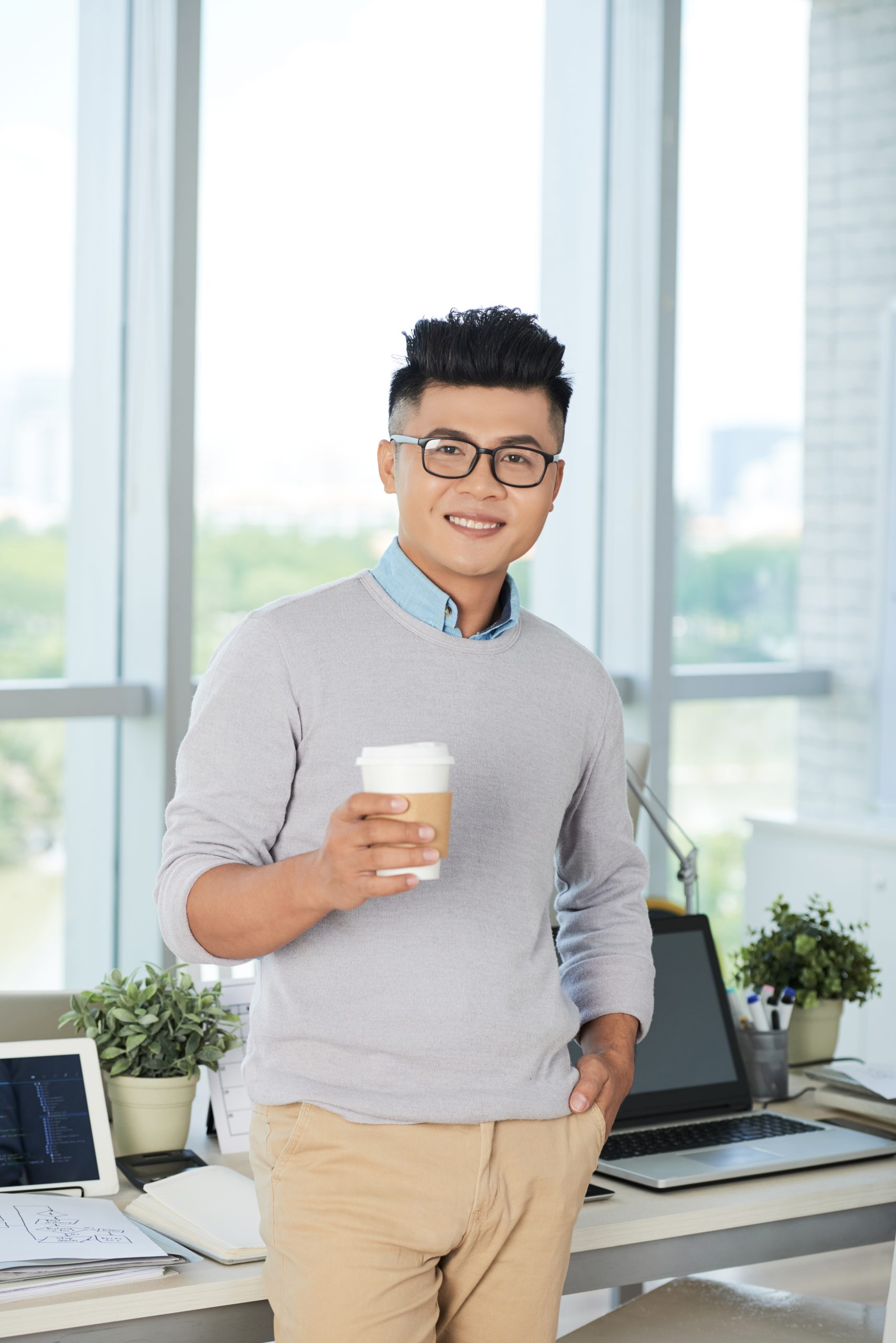 Portrait of young businessman in eyeglasses drinking coffee at office